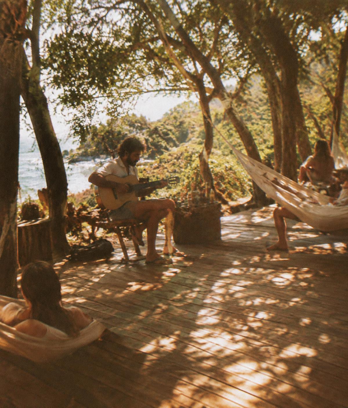 Acoustic guitarist on a shaded wooden deck with hammocks